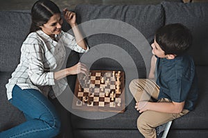 Young woman making a move in chess game while playing with her son on couch