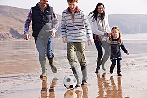 Family Playing Football On Winter Beach