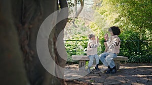 Family playing patty cake sitting park bench at weekend. African mom with girl