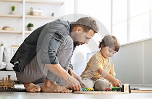 Family playtime. Happy interested father playing with little son, riding wooden toy train on railway, sitting on floor