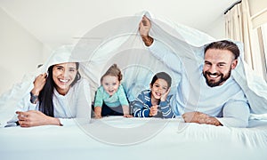Family, portrait and blanket fort in bed with children and parents, happy and playing in their home. Face, under and