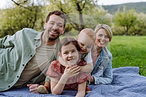 Family portrait with daughter and small toddler,, lying on picnic blanket outdoors in spring nature.