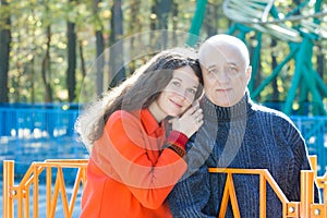 Family portrait of embracing adult daughter and her senior father at roller coaster amusement park background