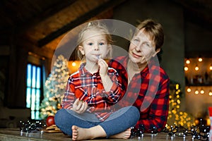 Family portrait of grandmother and granddaughter at home on Christmas morning with decorated Christmas tree with lights