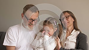 Family portrait - grandparents and grandchild having fun at home, together laughing. Grandfather sitting smiling while