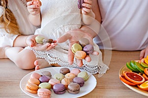 Family portrait of a happy mother, daughter and father posing in the kitchen during Breakfast, eating delicious macaroons, cakes,