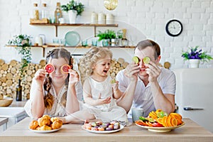 Family portrait of a happy mother  daughter and father posing in the kitchen during Breakfast  eating delicious macaroons  cakes 