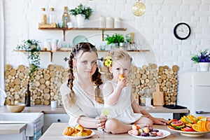 Family portrait of a happy mother and daughter posing in the kitchen during Breakfast  eating delicious macaroons  cakes  cookies