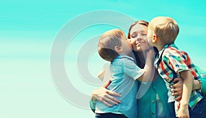 Family portrait, happy two children sons kissing their mom on a sunny day on blue sky background, Mothers day concept