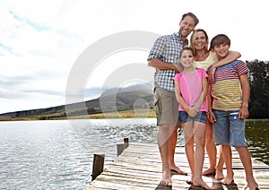 Family, portrait by lake and outdoor on pier for travel with vacation, parents and kids with fresh air in nature for