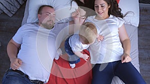 Family portrait of mom, dad and baby lying in bed at home, top view.