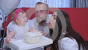 Family portrait mom, dad blowing candle on cake at baby girl`s first birthday.