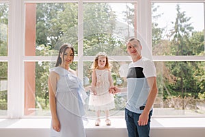 Family portrait of mom dand and little daughter in front of big window. Happy family