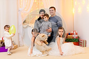 Family portrait - parents and children in home interior decorated with holiday lights and gifts