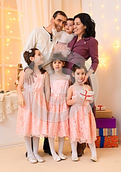 Family portrait of a parents and children in home interior decorated with lights and holiday gifts