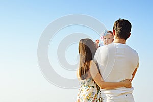 Family portrait. Picture of happy loving father, mother and their baby outdoors. Back view.