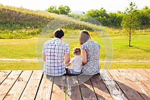 Family portrait. Picture of happy loving father, mother and their baby outdoors. Daddy, mom and child against green hill