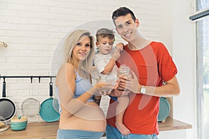 family portrait - pregnant mother, father and their little son standing in the kitchen, happy famile relatiosnhip