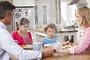 Family Praying Before Having Meal In Kitchen Together