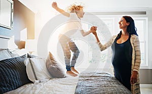 Family, pregnant woman and her son jumping on the bed while in their home together. Flare, love or smile and a boy child