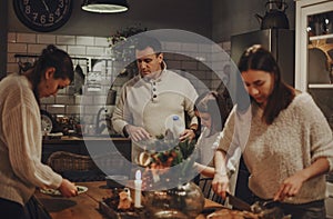 Family preparing festive Christmas Eve dinner together in cozy kitchen decorated for winter holidays