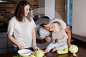 Family preparing healthy vegetable food in kitchen,mom cutting vegetables,child and dad having fun,biting bell pepper