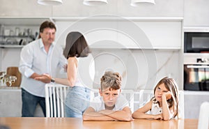 Family problem, conflict and people concept - sad children sitting at table their parents quarreling at home