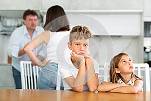 Family problem, conflict and people concept - sad children sitting at table their parents quarreling at home