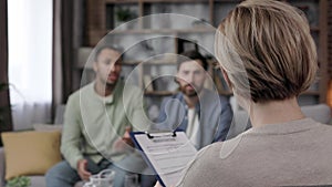 A family psychologist conducts a session in a beautiful office. LGBT couple at a psychotherapist's appointment