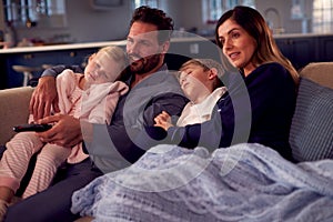 Family In Pyjamas Sitting On Sofa Watching TV Together As Children Fall Asleep