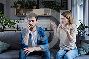 Family quarrel, man and woman sitting on sofa at home. angry woman yells at her husband, blames. The man is silent. He listens,