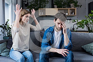 Family quarrel, man and woman sitting on sofa at home. angry woman yells at her husband, blames. The man is silent. He listens,