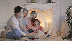 Family read book sitting on sofa in front of fireplace in Christmas decorated house interior