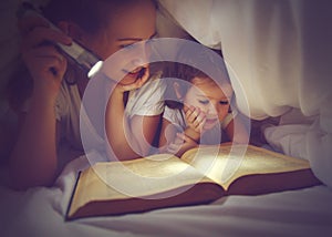 Family reading bedtime. Mom and child reading book with a flashlight under blanket