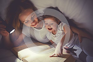 Family reading bedtime. Mom and child reading book with a flashlight under blanket