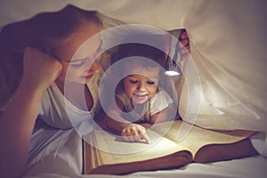 Family reading bedtime. Mom and child reading book with a flashlight under blanket