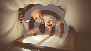 Family reading bedtime. Mom and child reading book with a flashlight under blanket