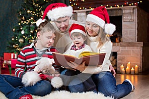 Family reading a book in front of Christmas tree