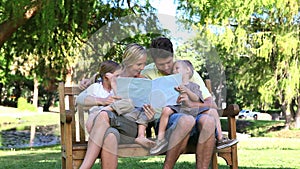 Family reading a book while sitting on a bench
