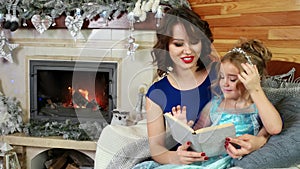 Family reading a Christmas story while sitting by the fireplace and Christmas tree, mother and daughter read a book, New