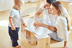 Family reading instruction and assemble furniture together at living room of new apartment pile of moving boxes on