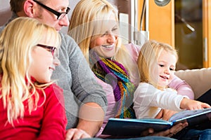 Family reading story in book on sofa in home