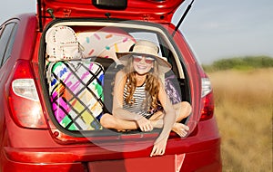 Family ready for the travel on summer vacation. Cute happy smiling little girl child is sitting in the red car with luggage and