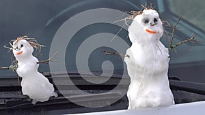 Family of real snowmen on windshield of car