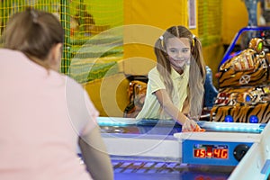 Family recreation concept. Happy teen girl playing air hockey with her mother at kids entertainment center