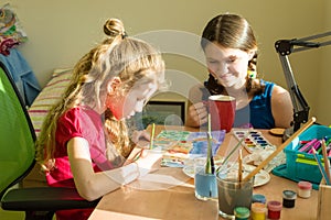 Family, recreation, creativity, home. Girls sisters at home, child is 7 years old draws watercolor at the table