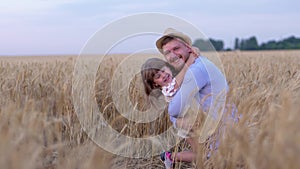 Family relationships, happy man cheerfully hugs little joyful girl and smile on field with ripe wheat during mature