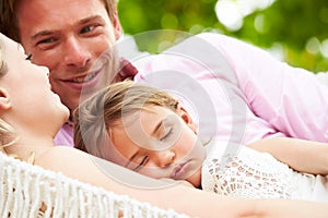 Family Relaxing In Beach Hammock With Sleeping Daughter