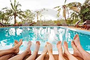 Family relaxing near swimming pool in hotel, feet of group of friends