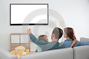 Family with remote control sitting on couch and watching TV at home, space for design on screen